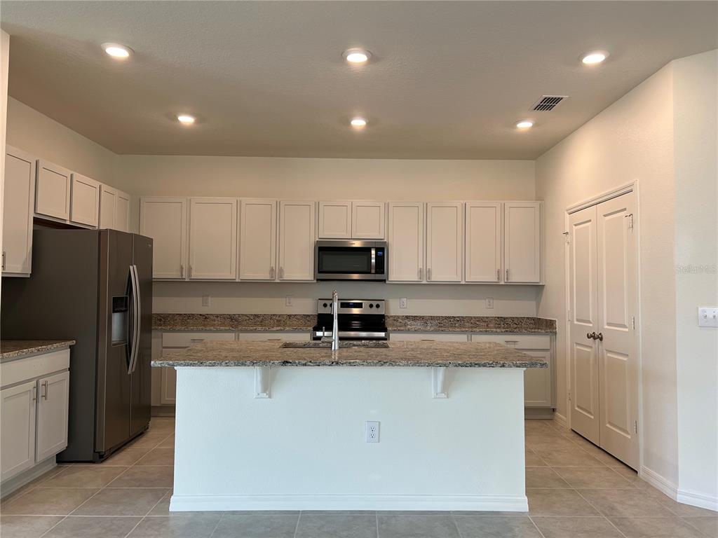 A kitchen features white cabinets, granite countertops, a center island, and stainless steel appliances — 9023 HOOTON WAY, DAVENPORT, FL