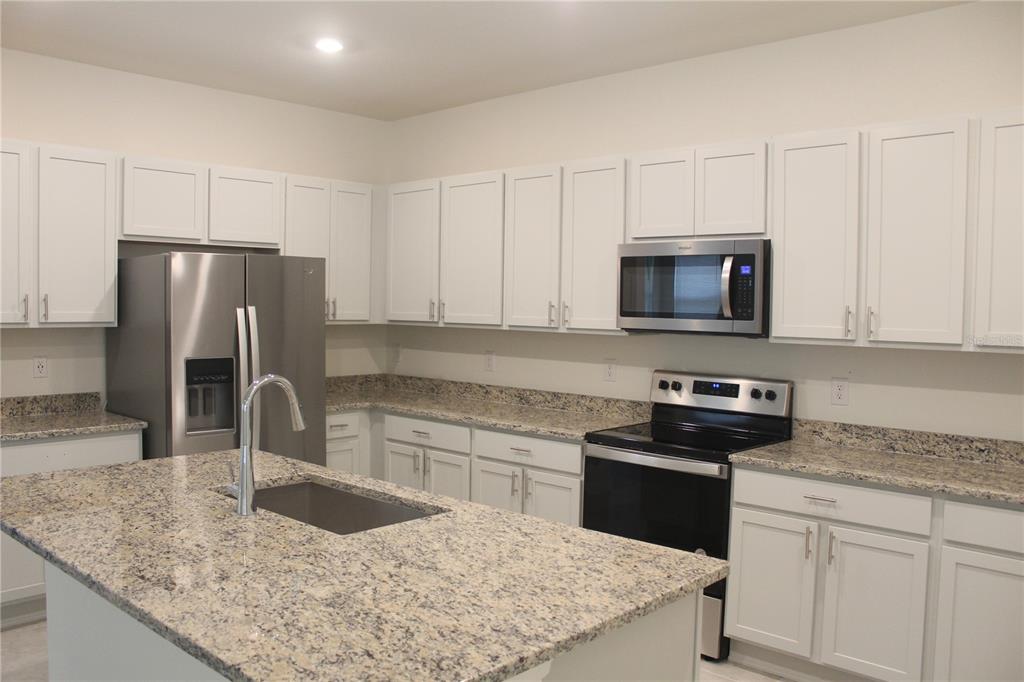 A kitchen features white cabinets, granite countertops, a stainless steel refrigerator, and a center island — 9023 HOOTON WAY, DAVENPORT, FL