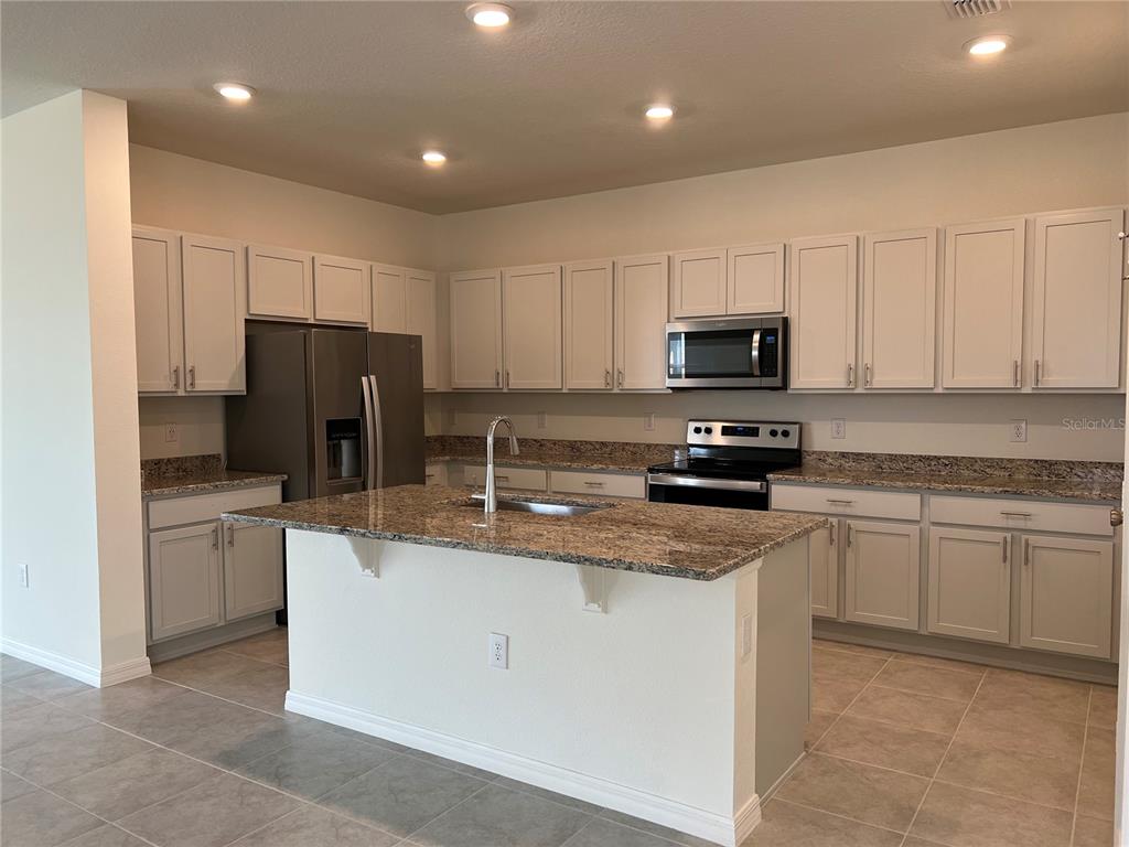 A kitchen features light gray cabinets, granite countertops, a center island, and stainless steel appliances — 9023 HOOTON WAY, DAVENPORT, FL
