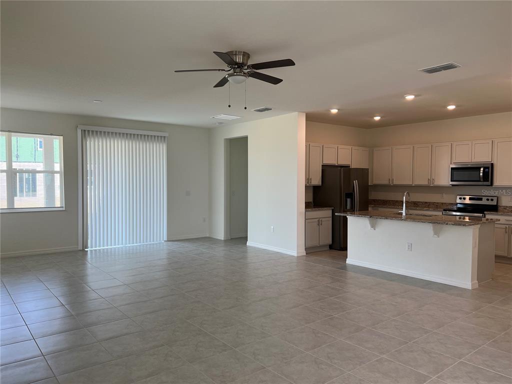 An open-concept living area features tile flooring, a ceiling fan, and an adjacent kitchen — 9023 HOOTON WAY, DAVENPORT, FL