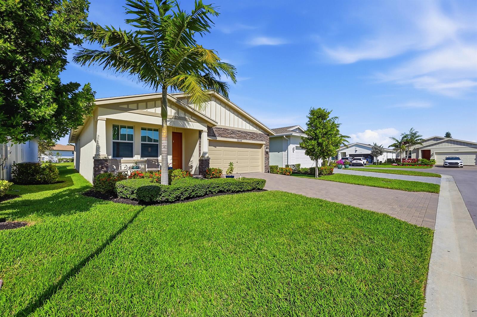 A single-story house with a beige exterior, stone accents, a palm tree, and a paved driveway — 5689 Graceful Way, Delray Beach FL 33484, DELRAY BEACH, FL