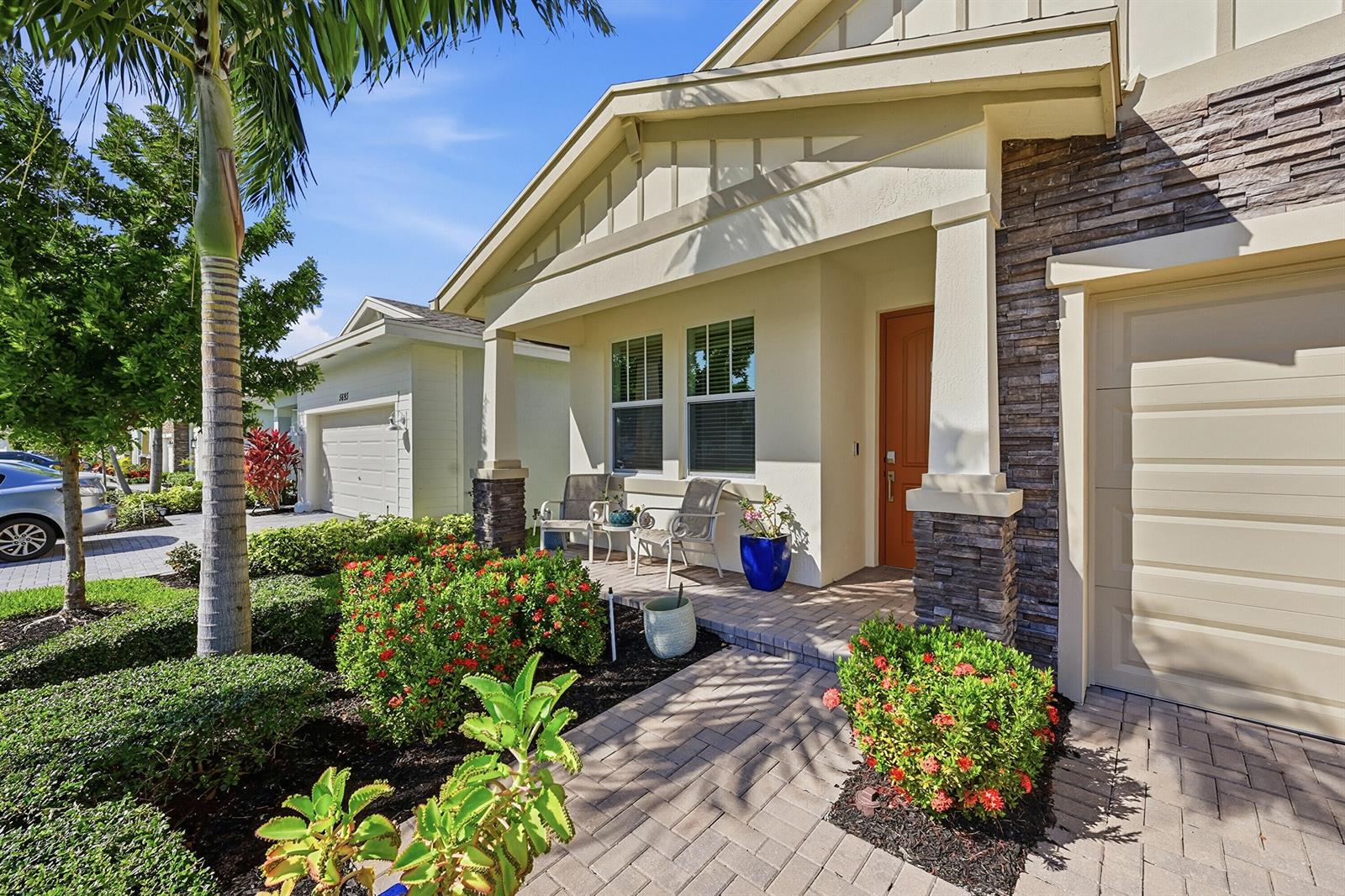A single-story house exterior features a stone-accented garage, a covered porch, and landscaped gardens — 5689 Graceful Way, Delray Beach FL 33484, DELRAY BEACH, FL