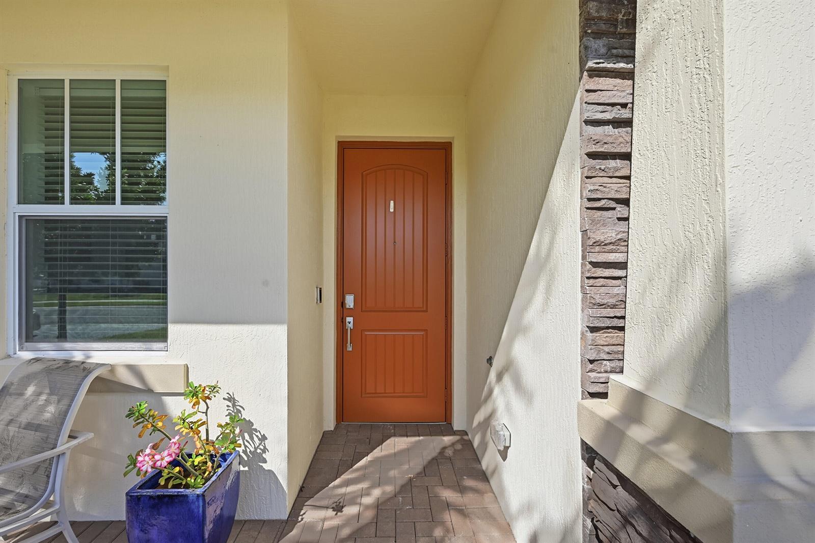A front entryway features a terracotta-colored door, a stone-accented wall, and a potted plant — 5689 Graceful Way, Delray Beach FL 33484, DELRAY BEACH, FL