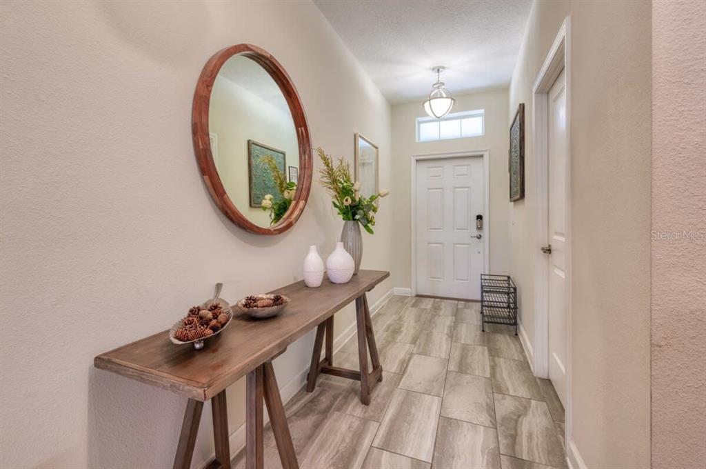 A foyer features a wooden console table, a round mirror, and light-colored tile flooring — 4793 KINGS CASTLE CIRCLE, KISSIMMEE, FL