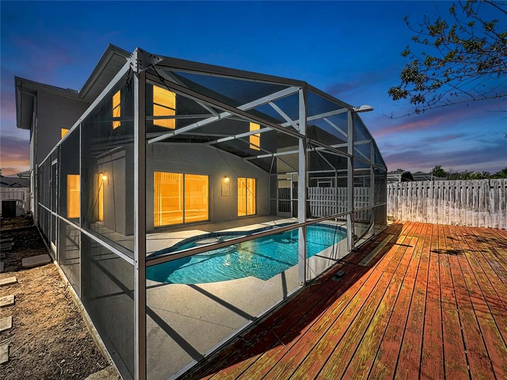 A screened-in swimming pool sits beside a wooden deck behind a house at dusk — 241 CORALWOOD COURT, KISSIMMEE, FL