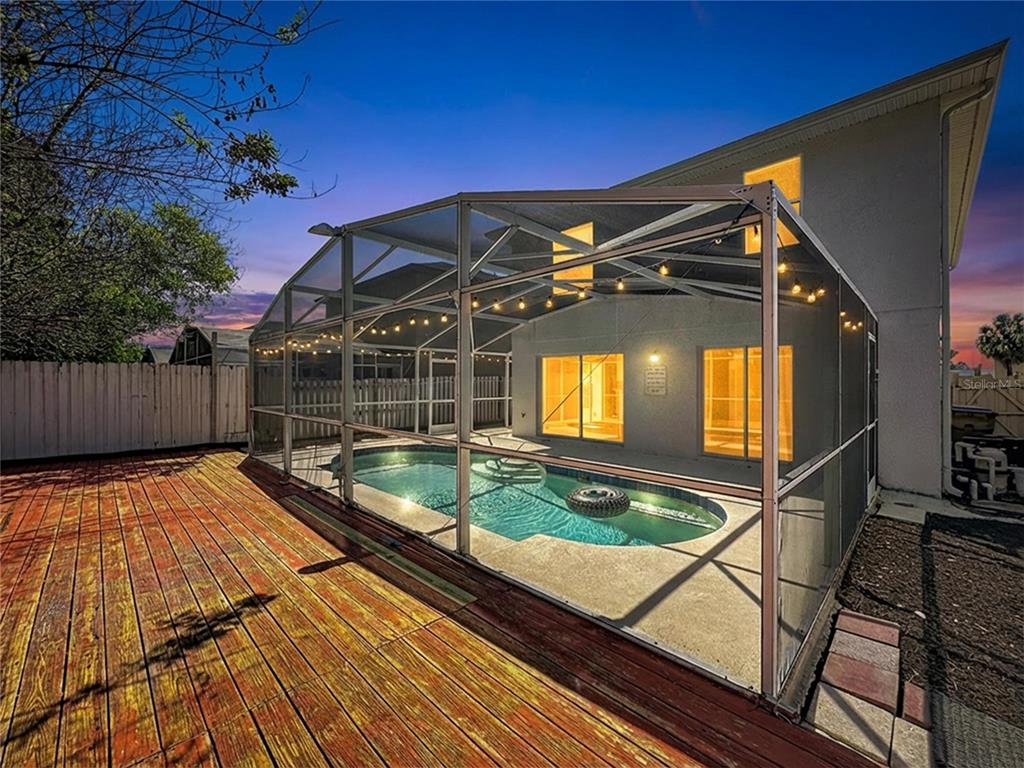 A backyard features a wooden deck and a screened-in swimming pool at dusk — 241 CORALWOOD COURT, KISSIMMEE, FL