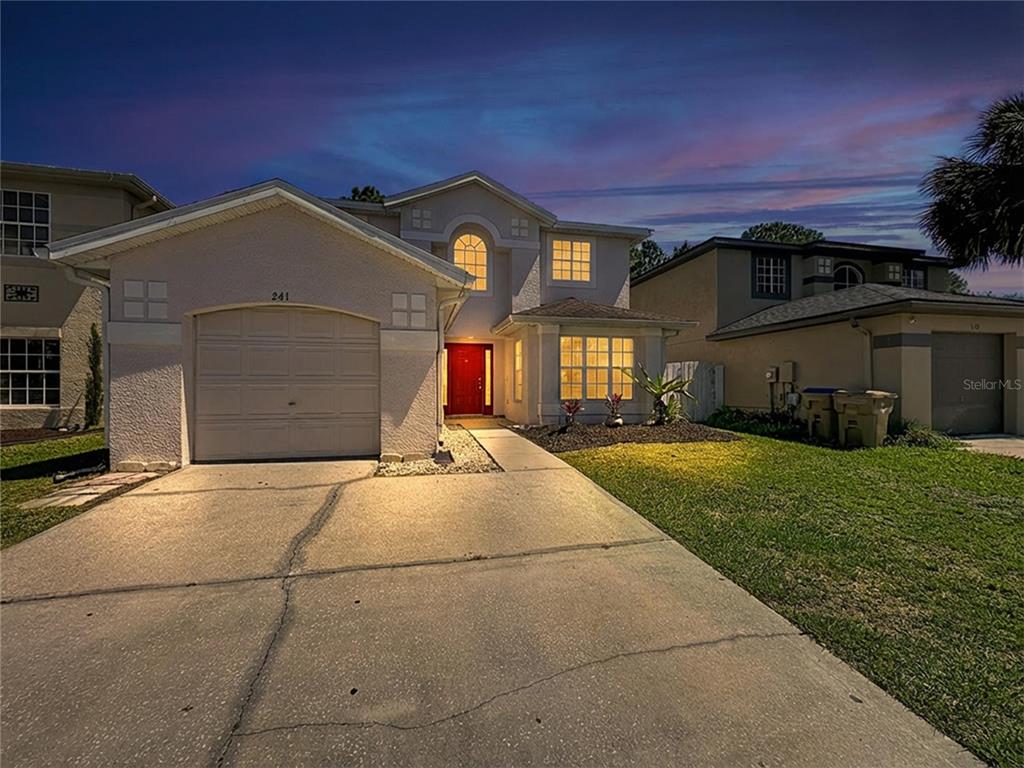 A two-story suburban house with a concrete driveway, a single-car garage, and a red door — 241 CORALWOOD COURT, KISSIMMEE, FL