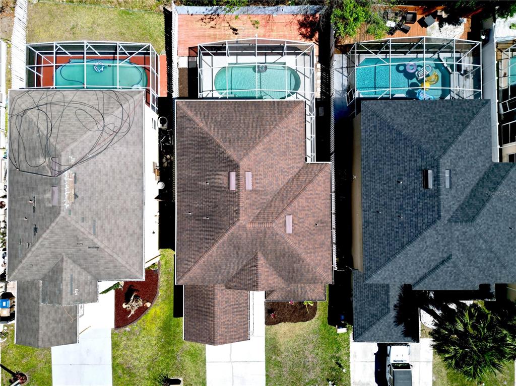 An aerial view shows three suburban houses with swimming pools enclosed by screened lanais — 241 CORALWOOD COURT, KISSIMMEE, FL