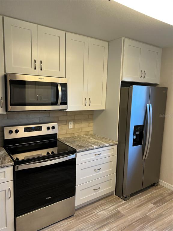 A kitchen features white cabinets, stainless steel appliances, a stone backsplash, and wood-look flooring — 175 KINGS HIGHWAY UNIT A8, PUNTA GORDA, FL