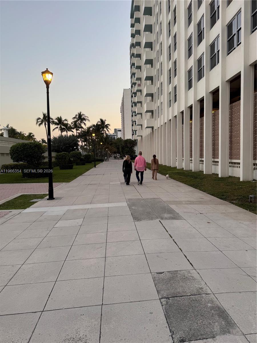 Three people walk with a small dog along a sidewalk beside a large apartment building — 2899 Collins Ave # 936, Miami Beach FL 33140, MIAMI BEACH, FL