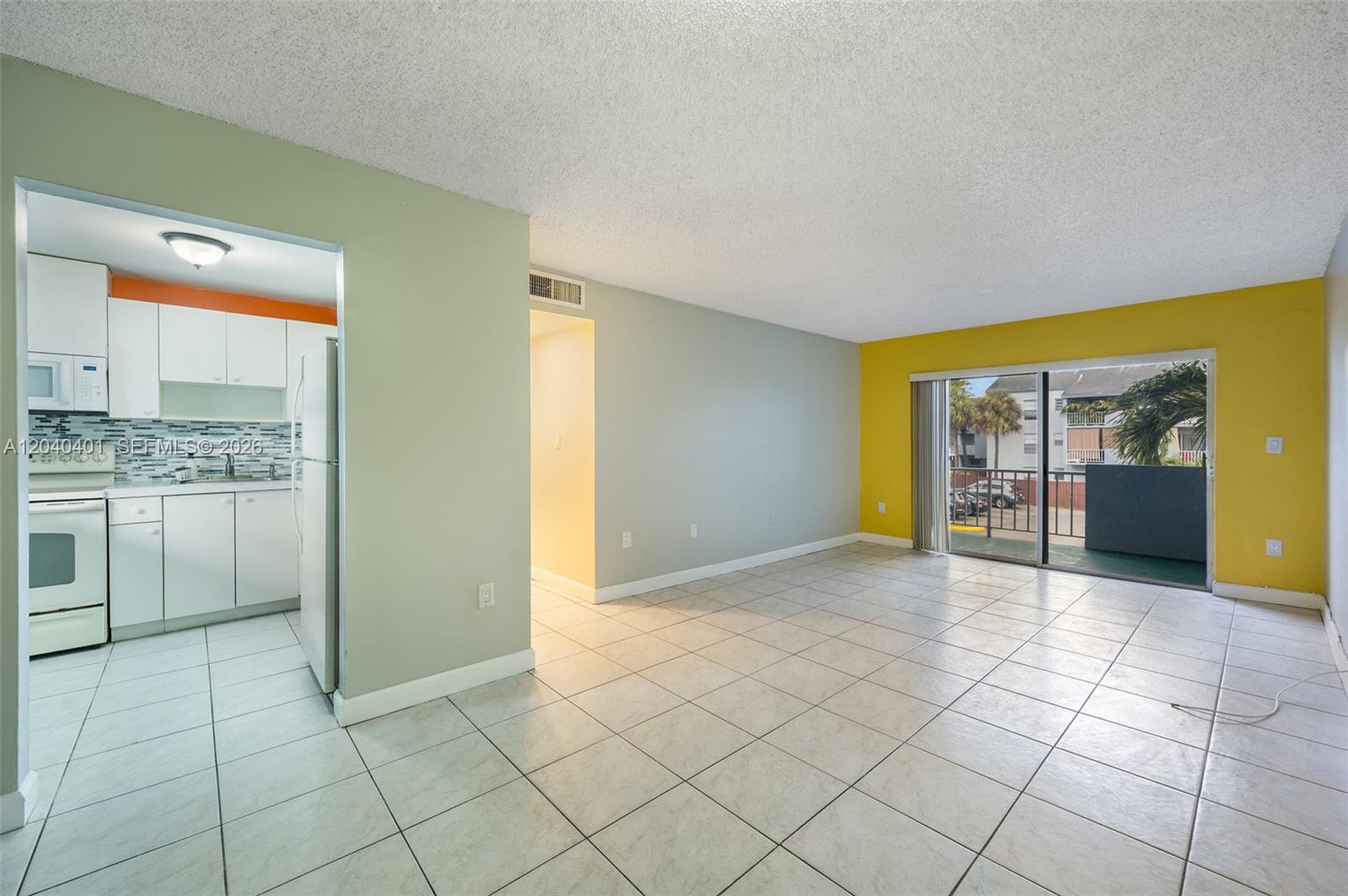 An open living area with tile floors features a yellow accent wall and sliding glass doors — 1725 W 60th St # F220, Hialeah FL 33012, HIALEAH, FL