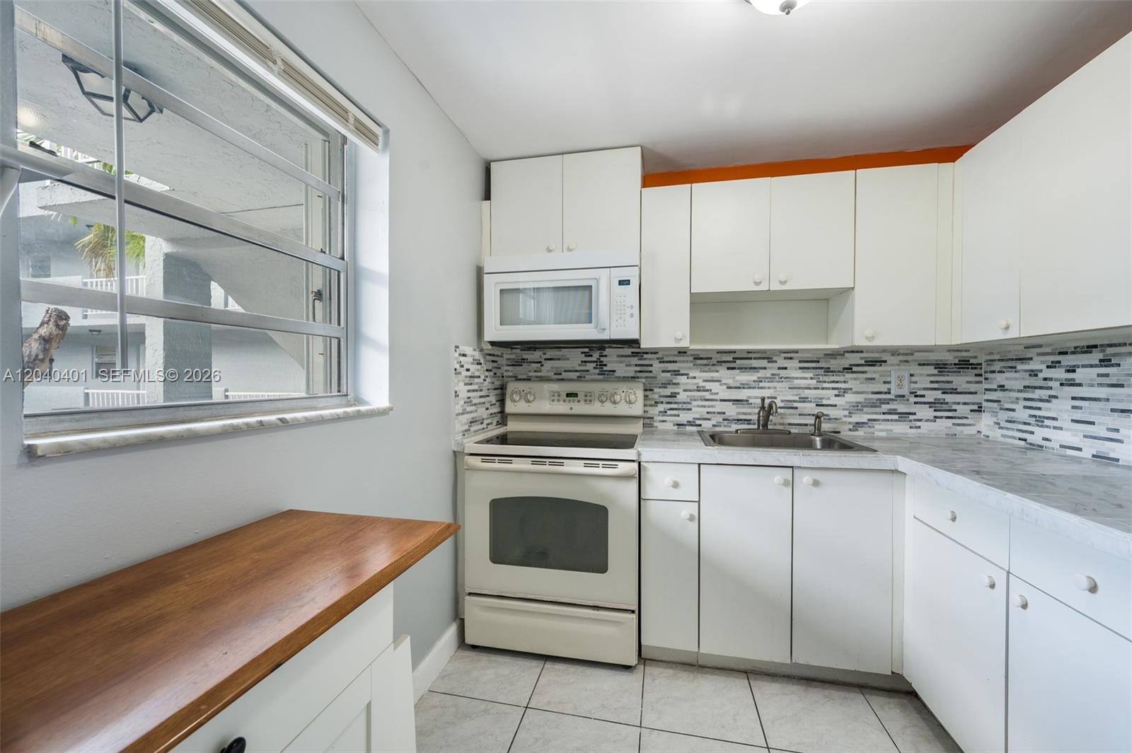 A small kitchen features white cabinets, a glass-top stove, and a mosaic tile backsplash — 1725 W 60th St # F220, Hialeah FL 33012, HIALEAH, FL
