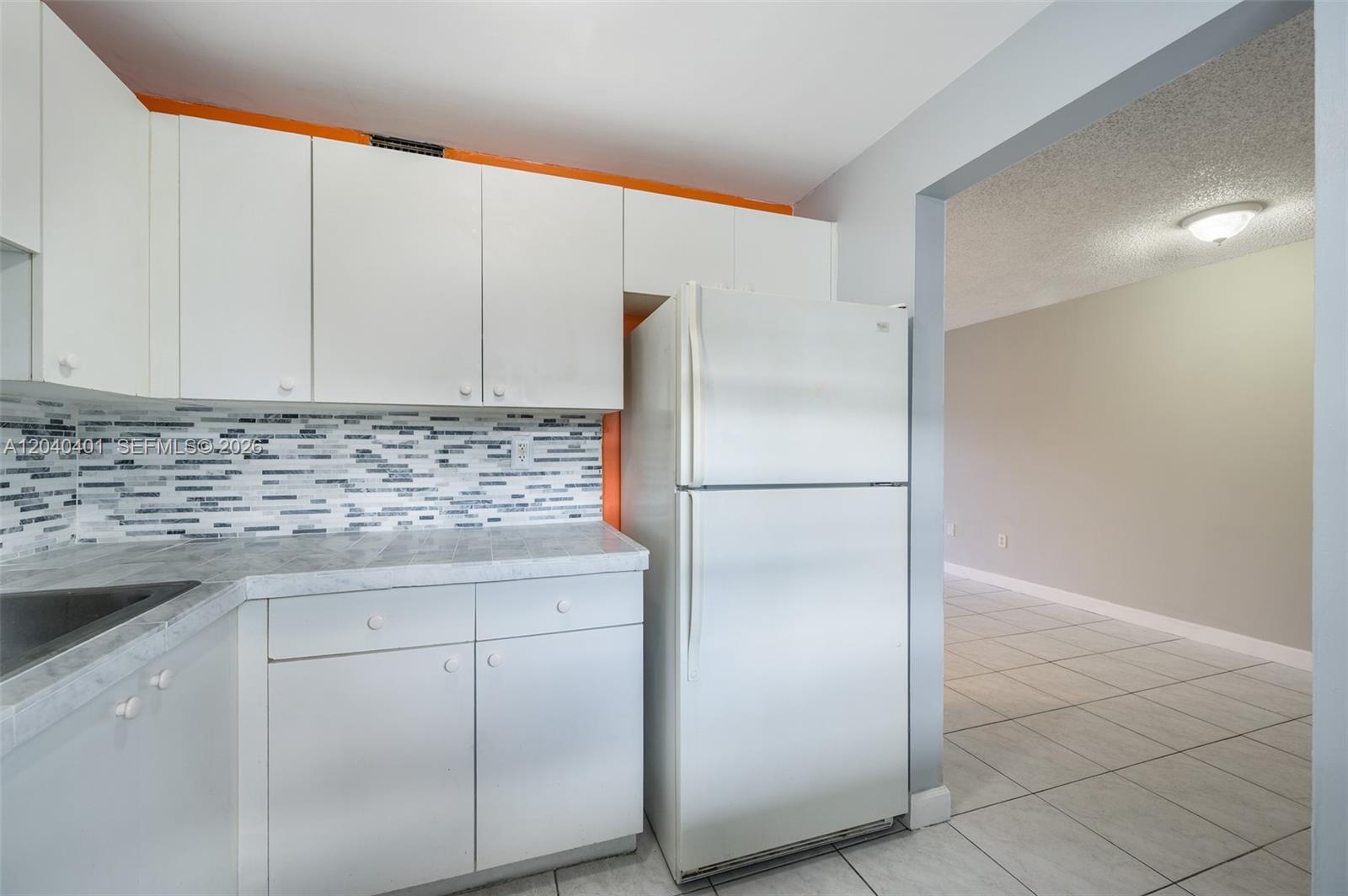 A kitchen features white cabinets, a marble-patterned countertop, a tiled backsplash, and a white refrigerator — 1725 W 60th St # F220, Hialeah FL 33012, HIALEAH, FL