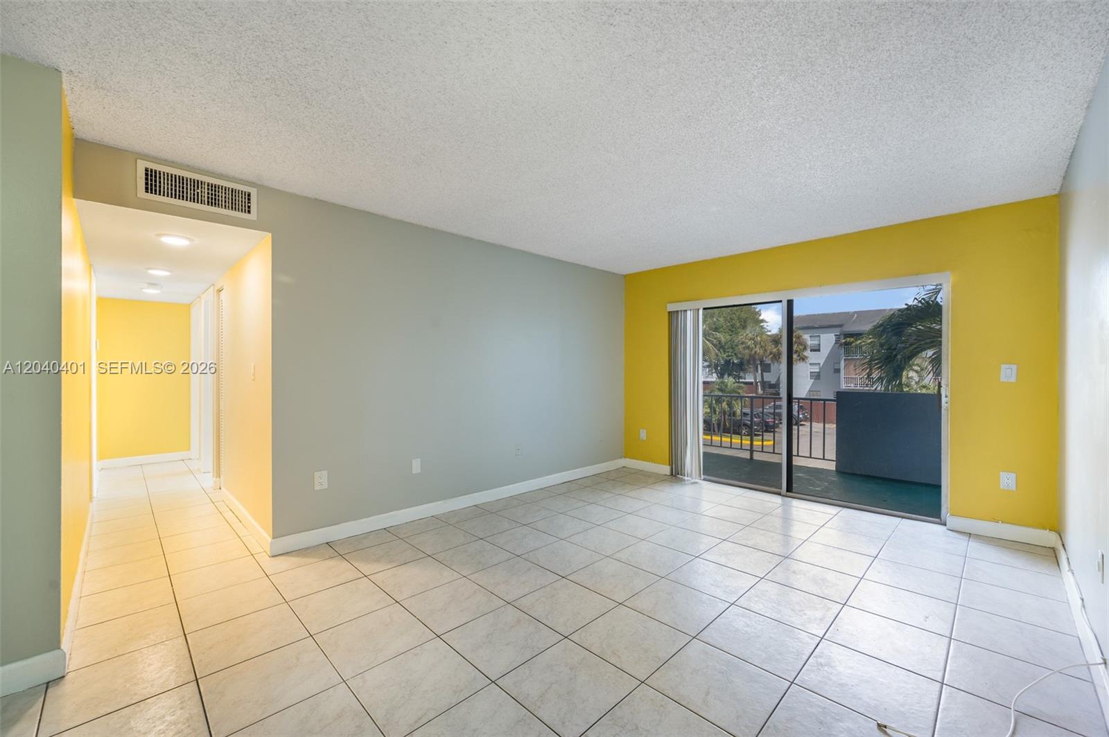 An empty living room features yellow and gray walls, tile flooring, and a sliding glass door — 1725 W 60th St # F220, Hialeah FL 33012, HIALEAH, FL