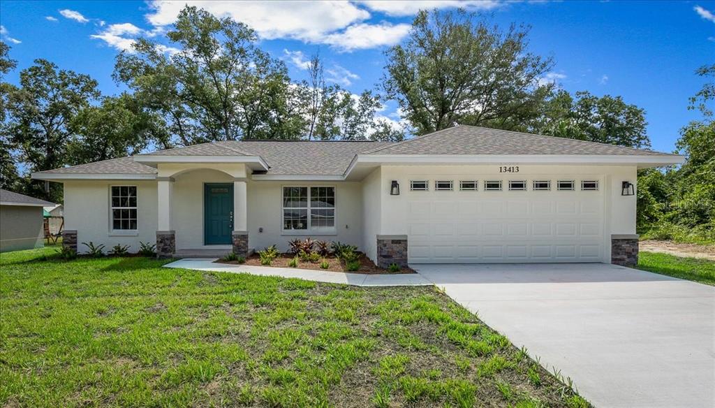 A single-story house with a white stucco exterior, stone accents, and a two-car garage — 13413 SE 101ST TERRACE, BELLEVIEW, FL