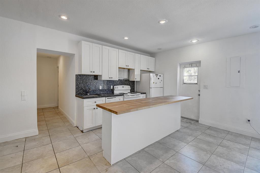 A kitchen features white cabinets, a dark granite countertop, and a wooden breakfast bar island — 707 SW 9th Court, Delray Beach FL 33444, DELRAY BEACH, FL