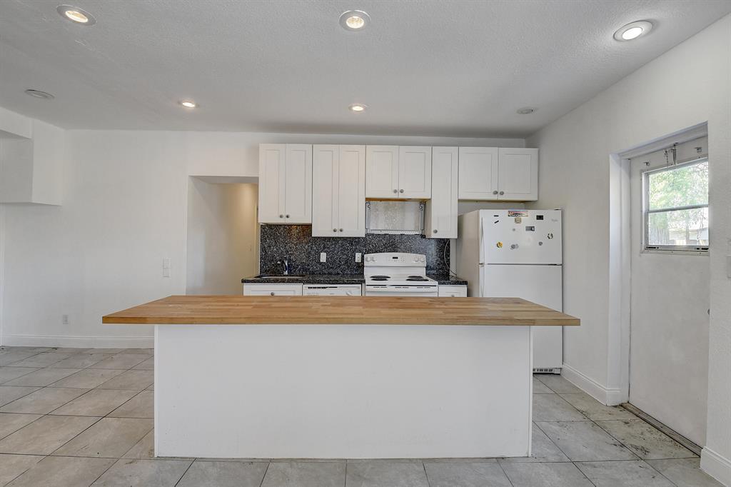 A kitchen features white cabinets, a butcher block island, dark countertops, and tile flooring — 707 SW 9th Court, Delray Beach FL 33444, DELRAY BEACH, FL