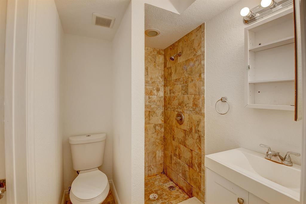 A bathroom features a toilet, a tiled walk-in shower, and a white vanity with shelving — 707 SW 9th Court, Delray Beach FL 33444, DELRAY BEACH, FL