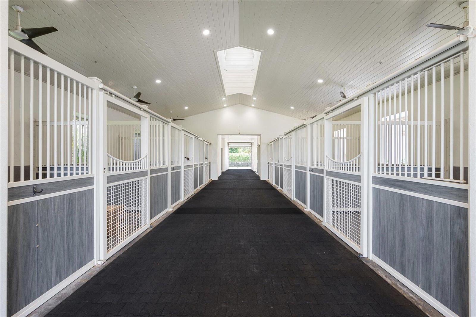 A bright, modern horse stable aisle features white stalls with grey wood-look panels and flooring — 15450 Estancia Lane, Wellington FL 33414, WELLINGTON, FL