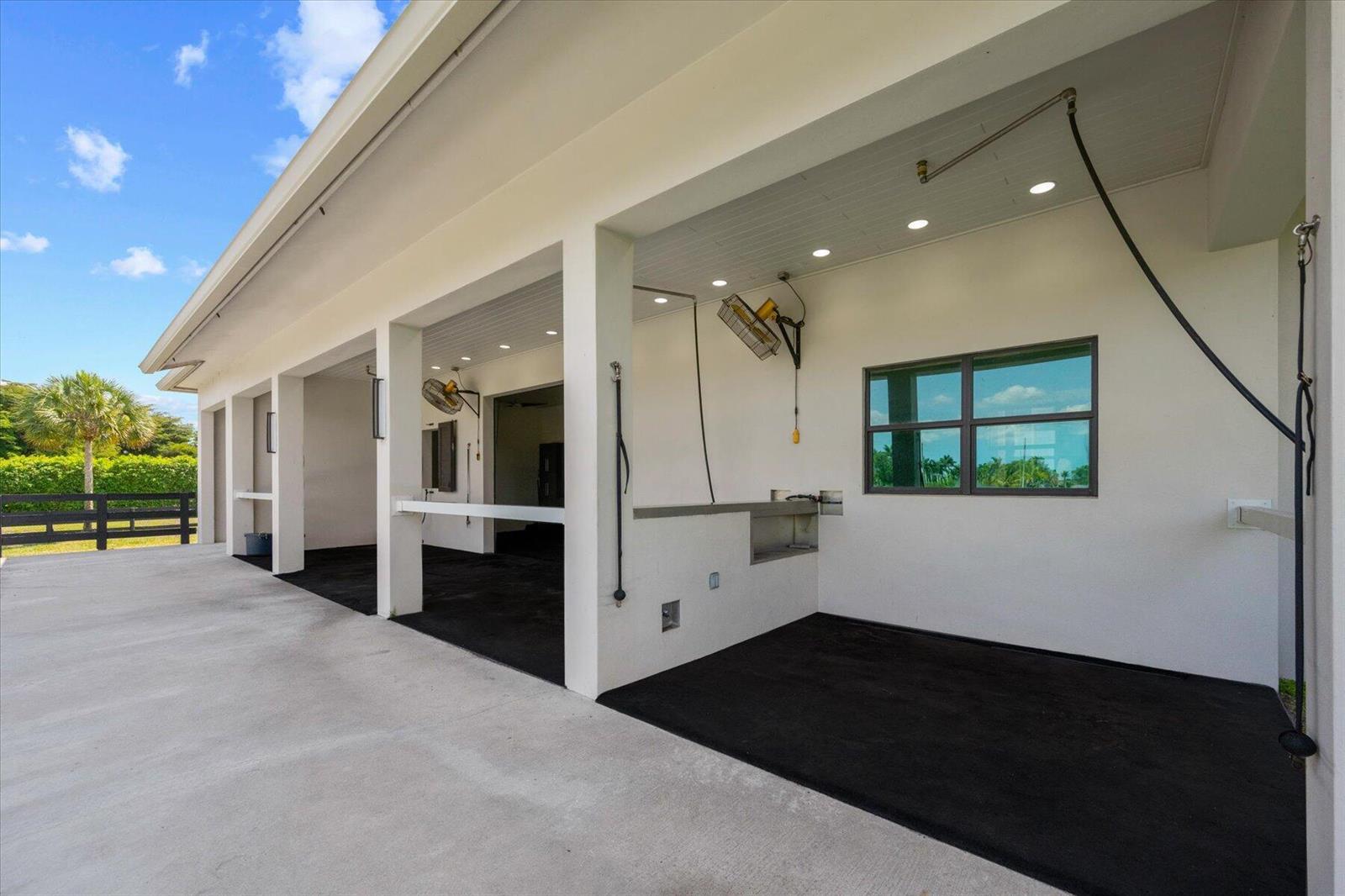 An outdoor horse wash stall area features concrete flooring, black rubber mats, and wall-mounted fans — 15450 Estancia Lane, Wellington FL 33414, WELLINGTON, FL