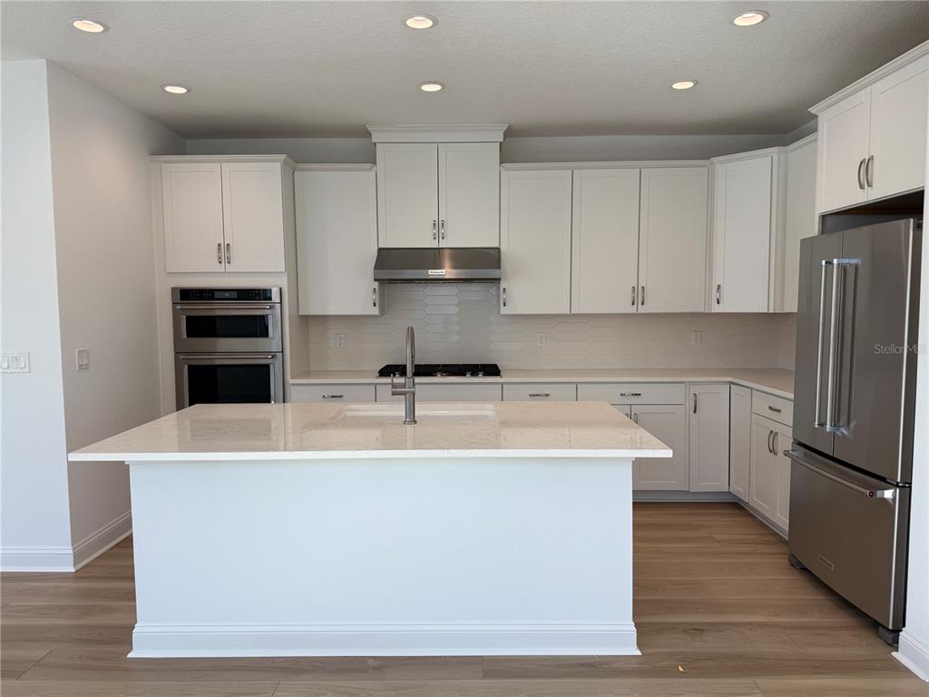 A modern kitchen features white cabinetry, stainless steel appliances, and a large central island — 9 WIMBLEDON WAY, PALM COAST, FL