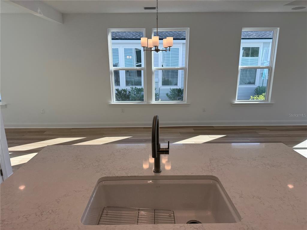 A kitchen island with a sink overlooks a dining area with three windows and lighting — 9 WIMBLEDON WAY, PALM COAST, FL