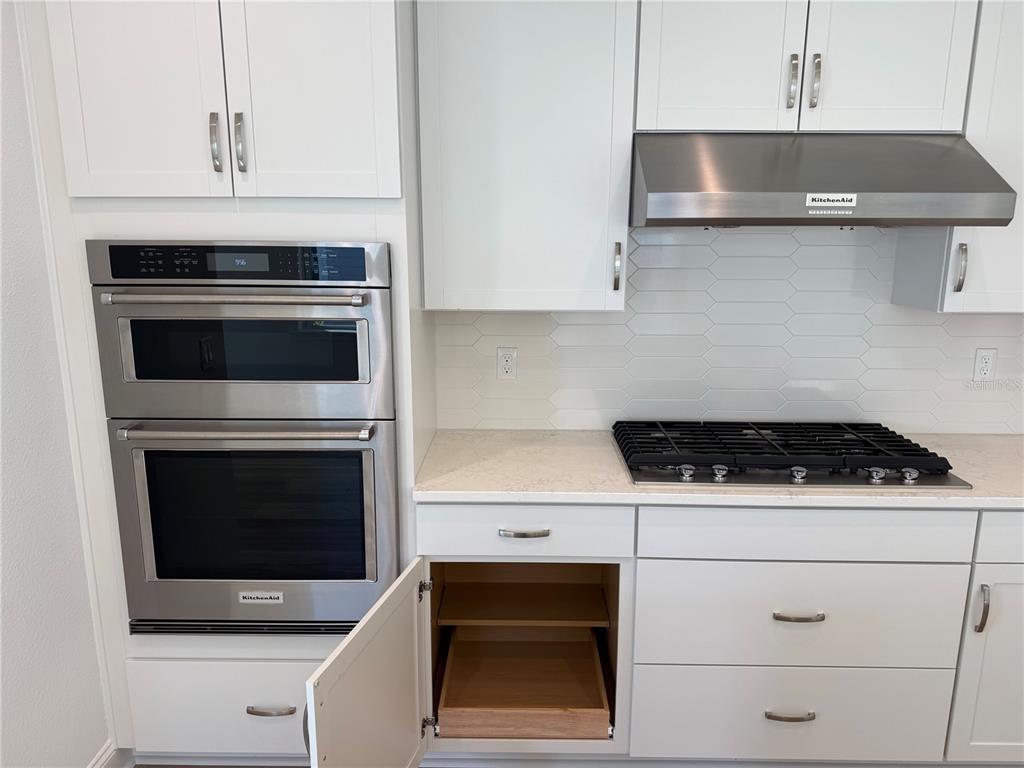 A modern kitchen features white cabinetry, stainless steel appliances, and a tiled backsplash — 9 WIMBLEDON WAY, PALM COAST, FL