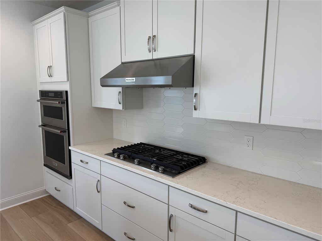A modern kitchen features white cabinets, a stainless steel range hood, and a gas cooktop — 9 WIMBLEDON WAY, PALM COAST, FL