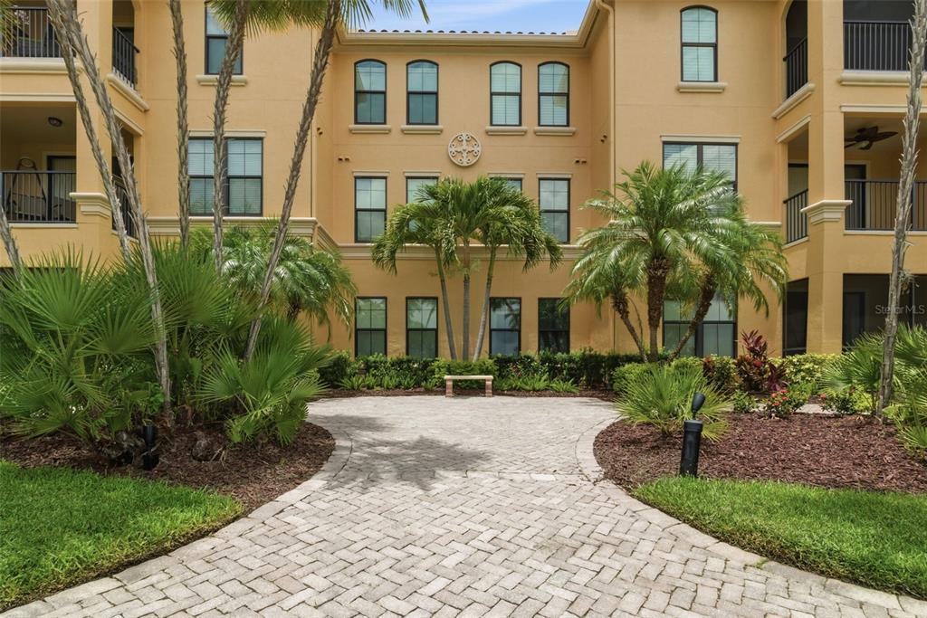 A paved walkway leads to a bench in front of a multi-story yellow apartment building — 2739 VIA CAPRI UNIT 1014, CLEARWATER, FL