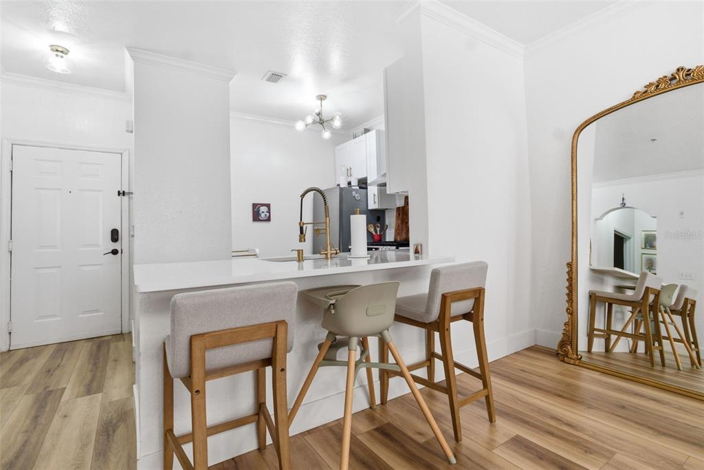 A kitchen features a white breakfast bar with three stools and light wood-look flooring — 2739 VIA CAPRI UNIT 1014, CLEARWATER, FL