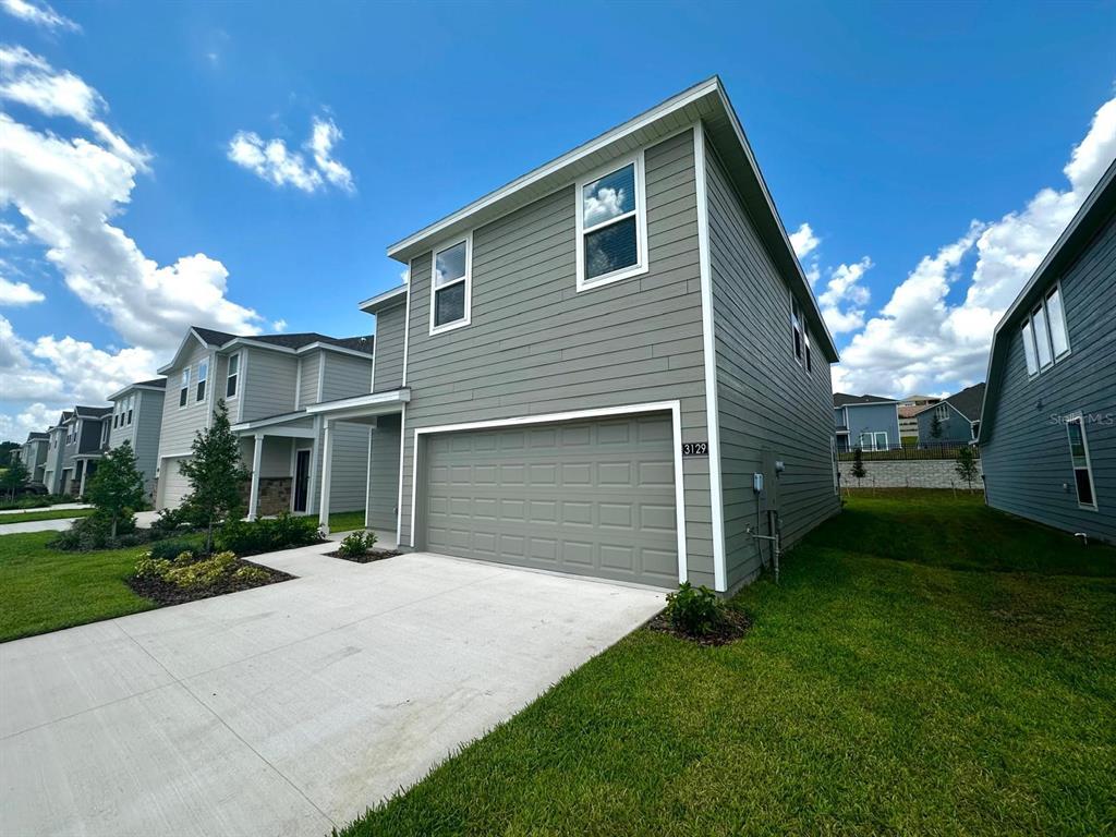 A two-story house with gray horizontal siding and a two-car garage under a blue sky — 3129 BROOKHOLLOW WAY, MINNEOLA, FL