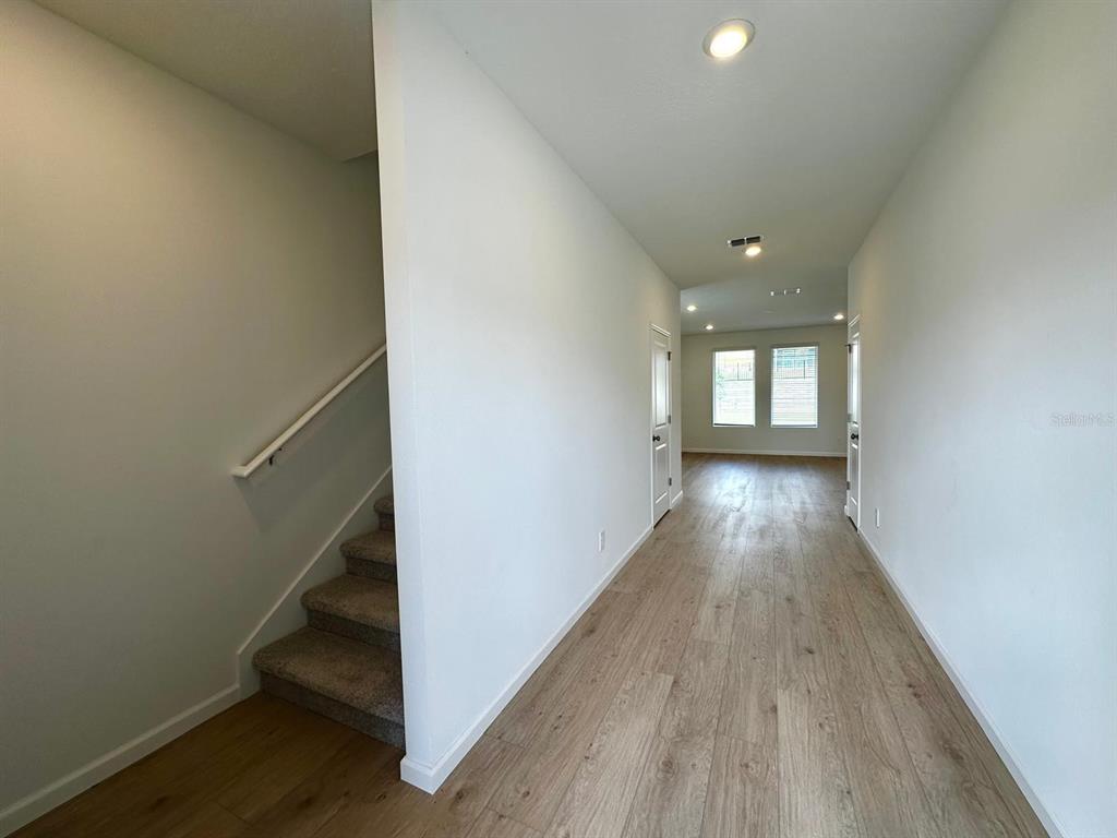A hallway with light wood flooring leads to a room with windows and stairs — 3129 BROOKHOLLOW WAY, MINNEOLA, FL