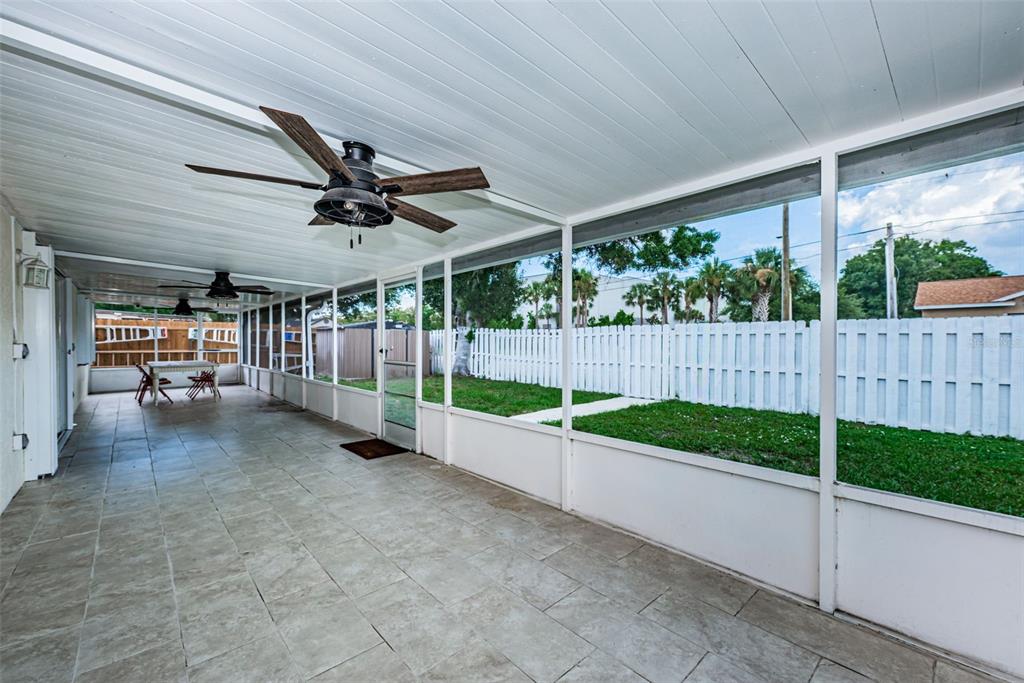 A covered, tiled patio features ceiling fans and a screened-in view of a fenced backyard — 8419 125TH PLACE, LARGO, FL