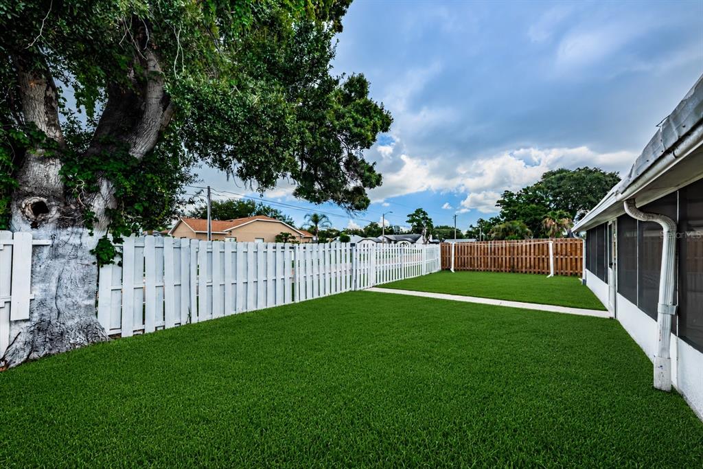 A backyard with artificial turf, a white vinyl fence, and a large tree — 8419 125TH PLACE, LARGO, FL