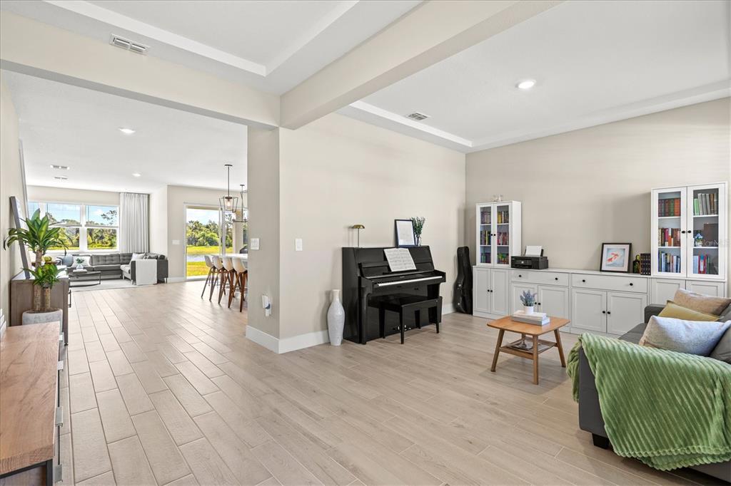 A living room with light wood-look tile floors, a black piano, and built-in white cabinetry — 506 SUN CHASER DRIVE, NOKOMIS, FL