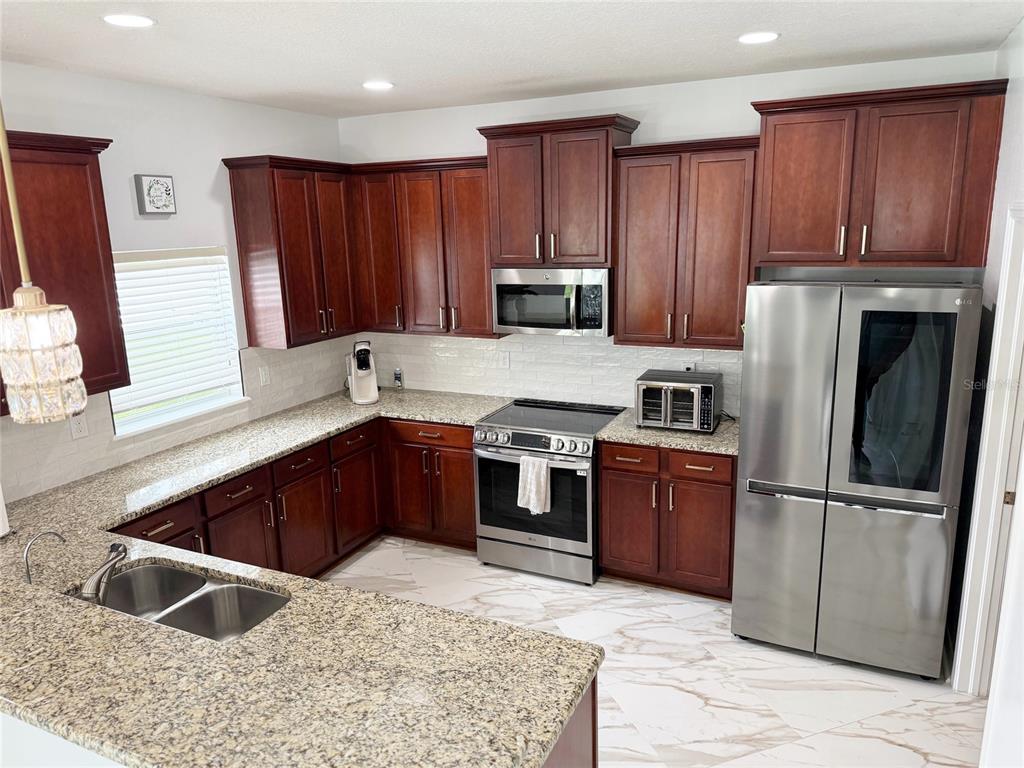 A kitchen features dark wood cabinets, granite countertops, stainless steel appliances, and white tile flooring — 12236 FAIRLAWN DRIVE, RIVERVIEW, FL