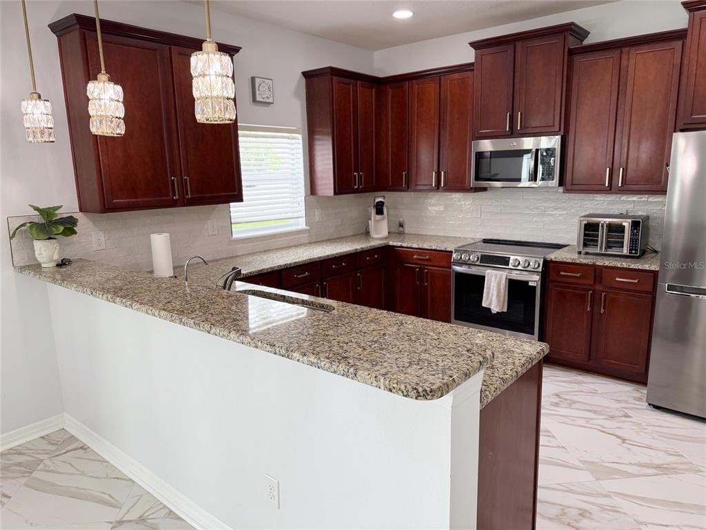 A kitchen features dark wood cabinets, granite countertops, stainless steel appliances, and light tile flooring — 12236 FAIRLAWN DRIVE, RIVERVIEW, FL