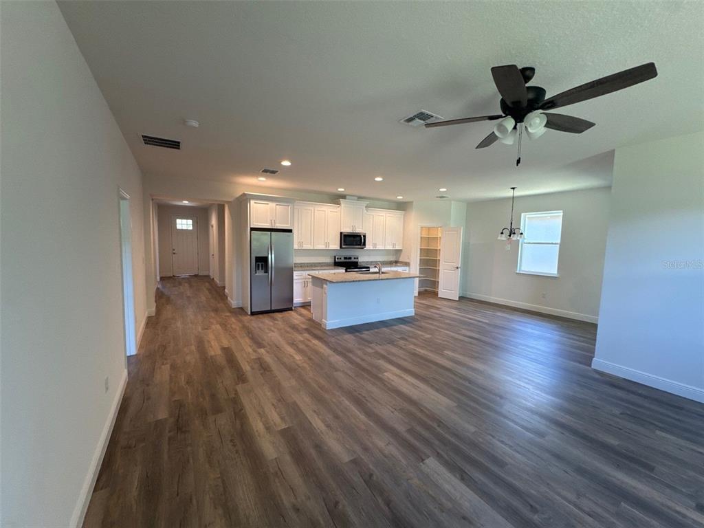 An open-concept kitchen and living area featuring white cabinetry, a kitchen island, and wood-look flooring — 519 ELLIE COURT, APOPKA, FL