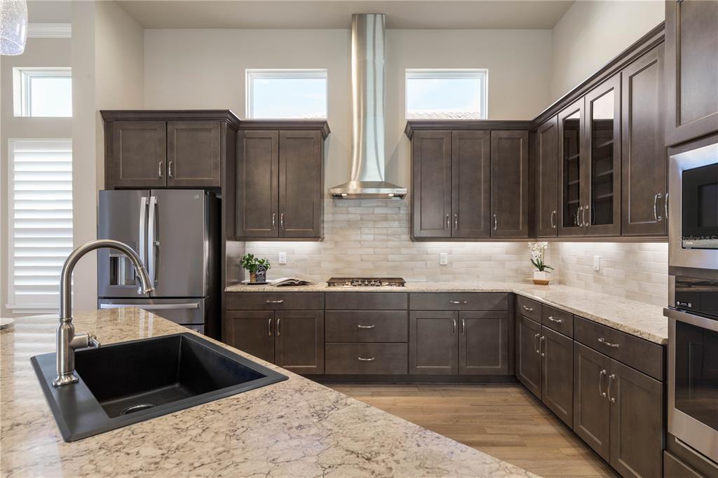 A modern kitchen features dark wood cabinets, granite countertops, a stainless steel hood, and island — 661 MAHOGANY RUN, PALM COAST, FL