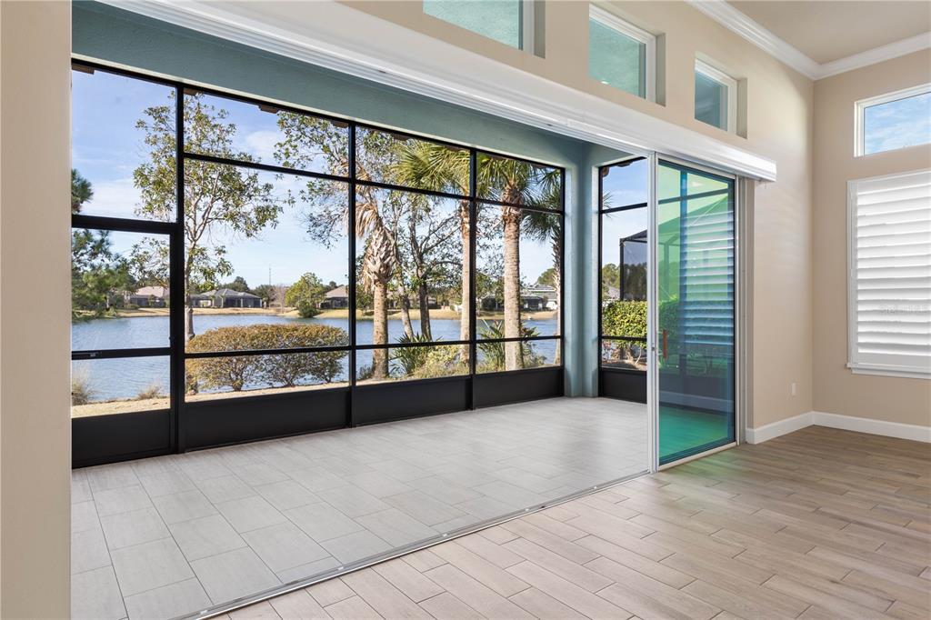 A sunroom with tile flooring features large sliding glass doors opening to a lake view — 661 MAHOGANY RUN, PALM COAST, FL
