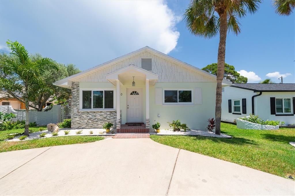 A light green single-story house features a stone facade, white trim, and a palm tree — 150 42ND AVENUE, ST PETE BEACH, FL