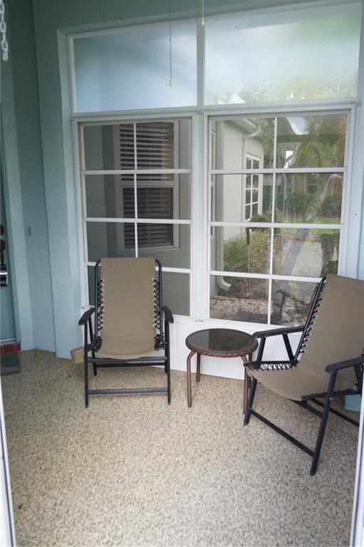 A covered patio features two folding chairs, a small side table, and large window panels — 652 MC DANIEL STREET UNIT 90, SUN CITY CENTER, FL