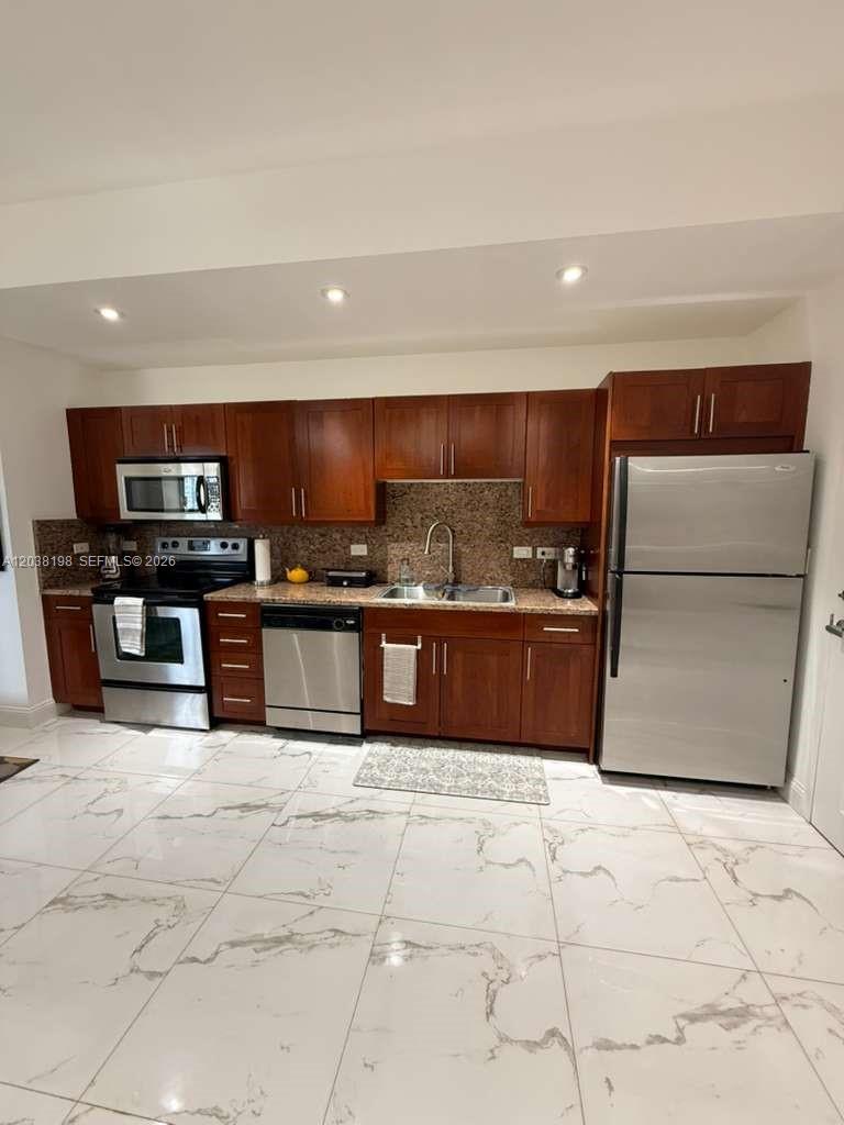 A kitchen features cherry wood cabinets, stainless steel appliances, and white marble-patterned tile flooring — 111 E Flagler St # 806, Miami FL 33131, MIAMI, FL