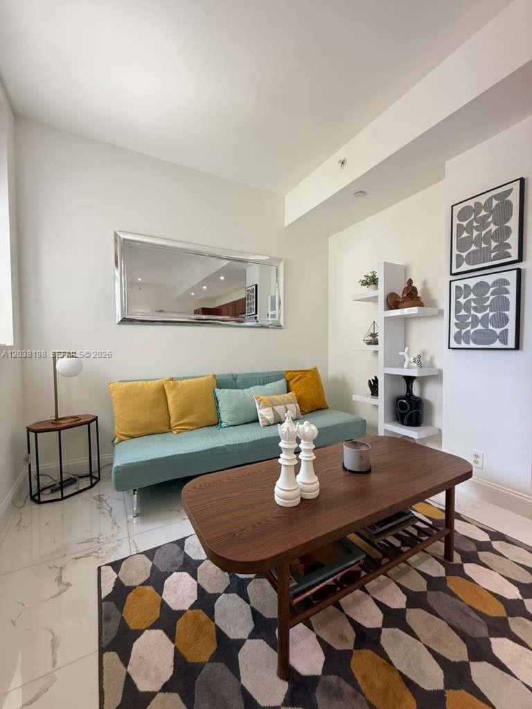 A living room features a teal sofa, a wooden coffee table, and geometric wall art — 111 E Flagler St # 806, Miami FL 33131, MIAMI, FL