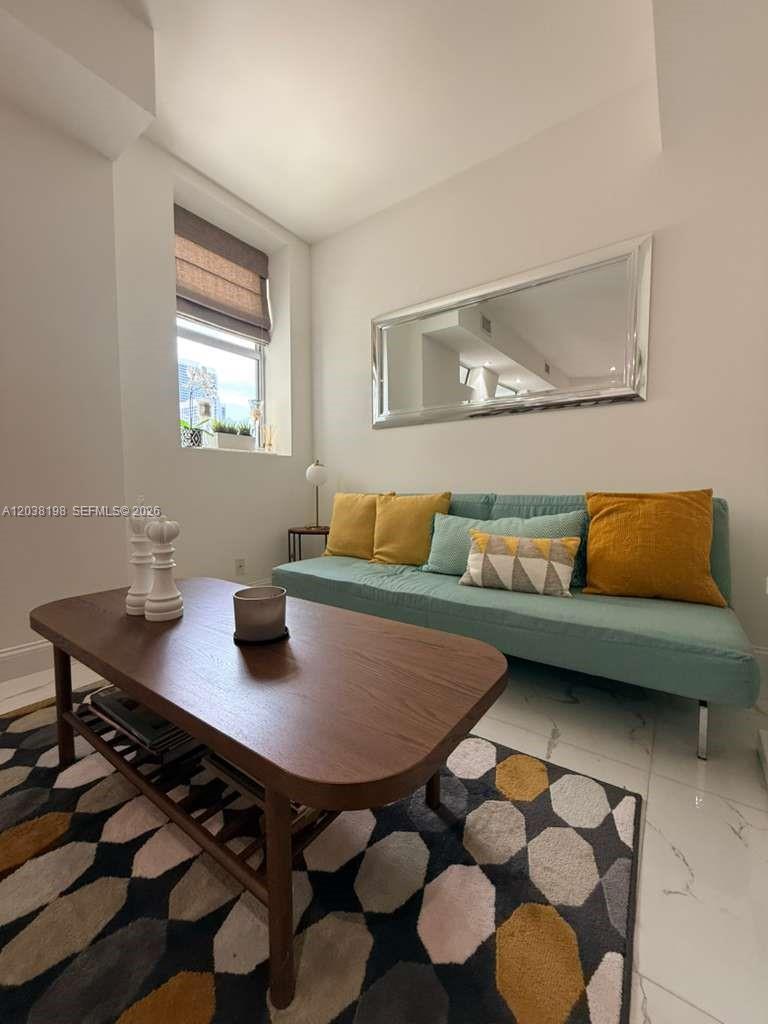 A living room features a teal sofa, a wooden coffee table, and a geometric area rug — 111 E Flagler St # 806, Miami FL 33131, MIAMI, FL