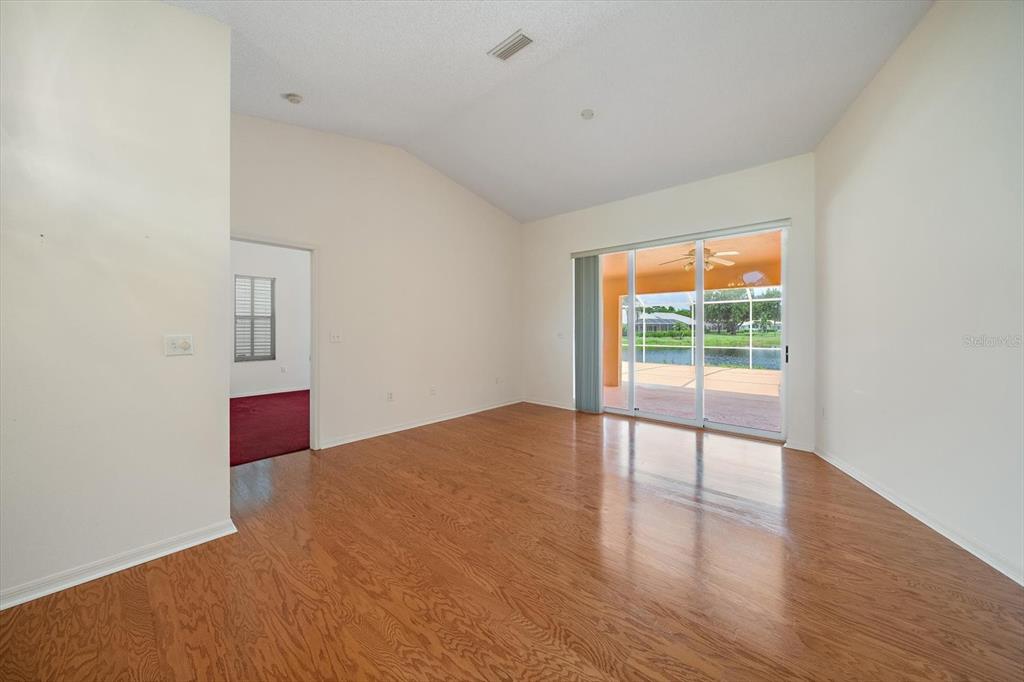 An empty room with hardwood floors, vaulted ceilings, and sliding glass doors leading to a patio — 9539 HAWKSMOOR LANE, SARASOTA, FL