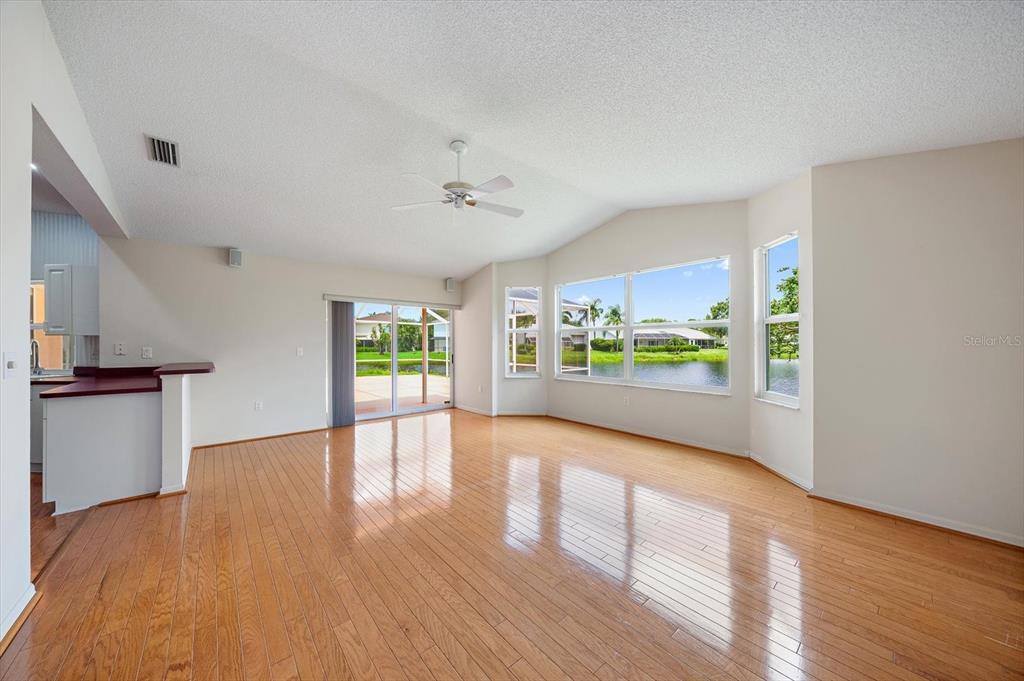 An empty living room with hardwood floors, a ceiling fan, and large windows overlooking water — 9539 HAWKSMOOR LANE, SARASOTA, FL