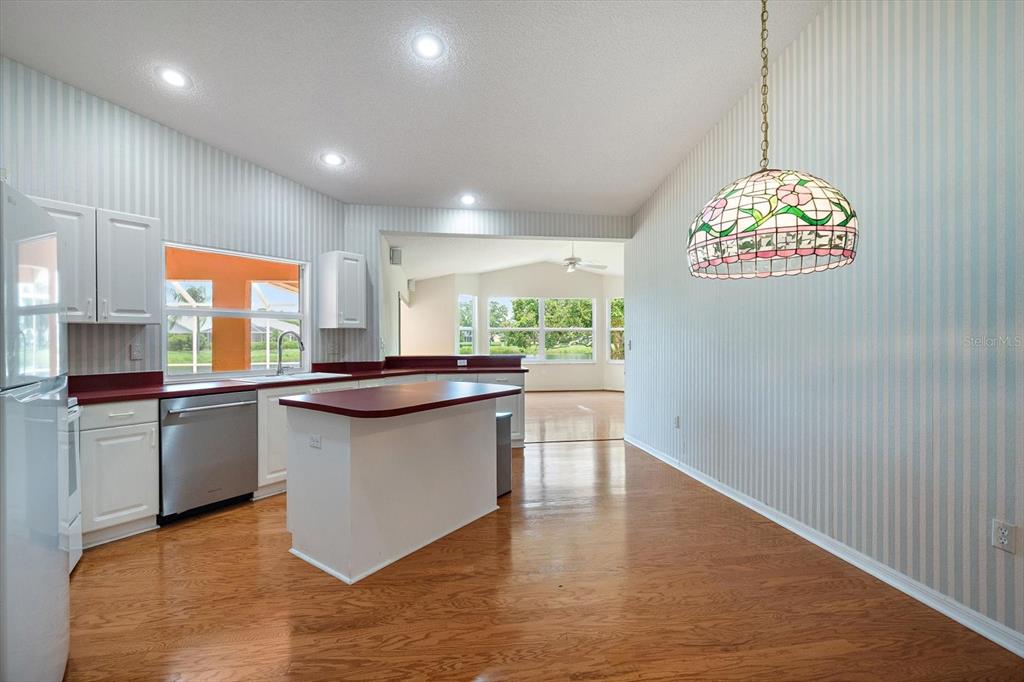 A kitchen with white cabinets, red countertops, and a stained-glass pendant light over hardwood floors — 9539 HAWKSMOOR LANE, SARASOTA, FL
