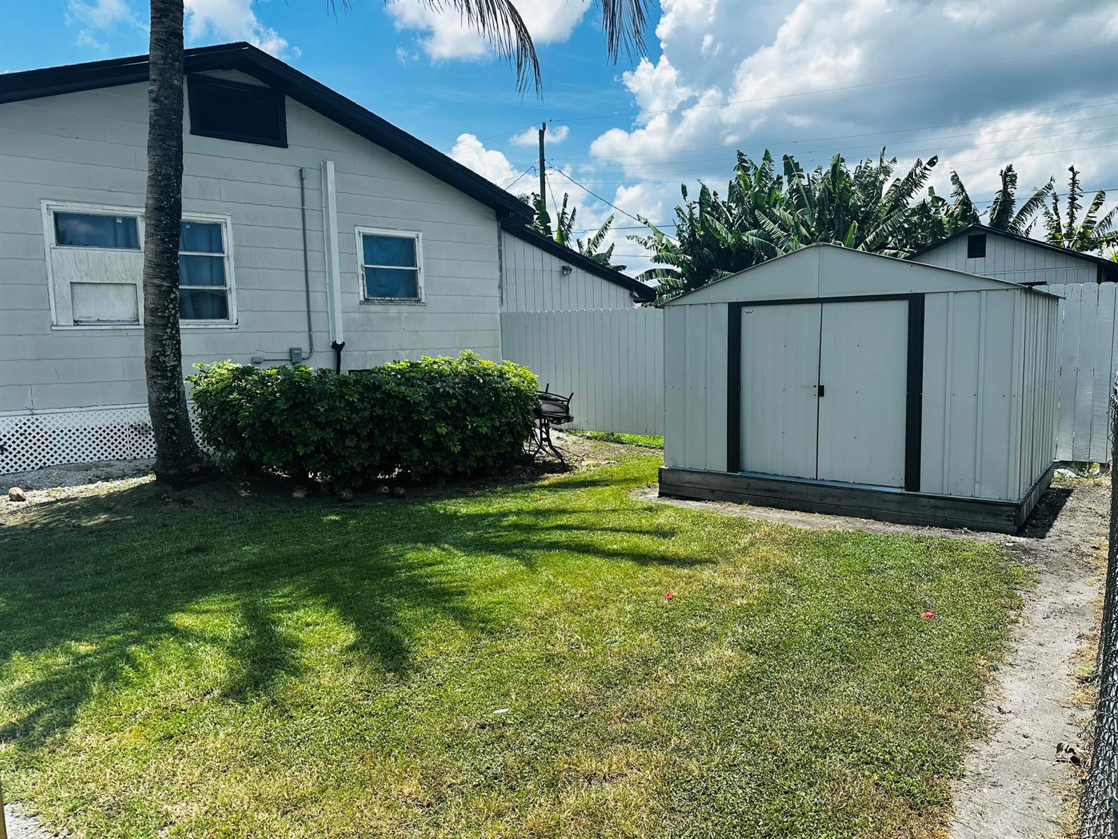 A backyard features a white house, a metal storage shed, and a green lawn — 566 SE 7th Drive, Belle Glade FL 33430, BELLE GLADE, FL