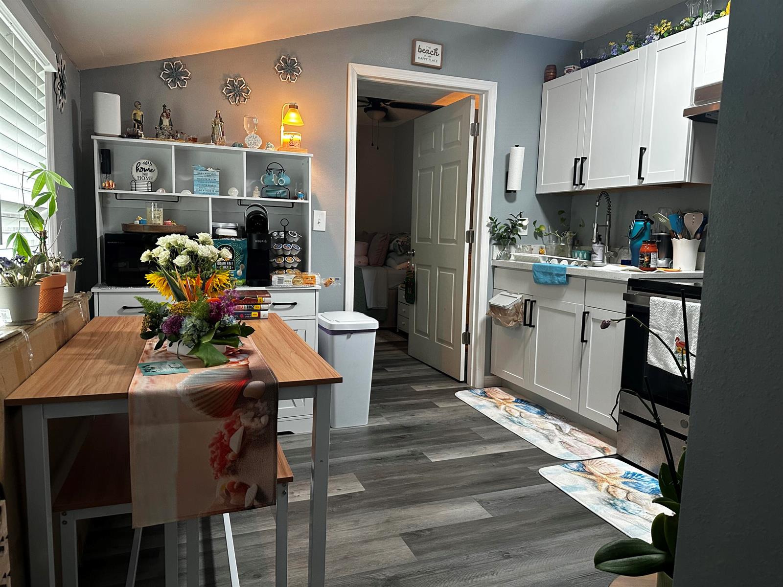 A kitchen with white cabinets, wood-look flooring, and a dining table with a floral centerpiece — 566 SE 7th Drive, Belle Glade FL 33430, BELLE GLADE, FL